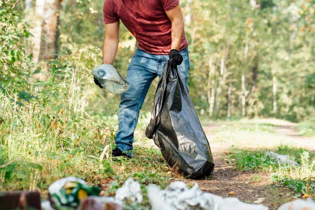 IMAGO Nature: Unsere Erde, Umweltverträgliche Herausforderungen, Plastikmüll Mid adult male environmentalist putting plastic bottle in garbage bag model released, VPIF05096
