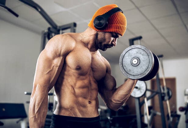 Strong confident muscular Hispanic male athlete listening playlist in wireless headphones while doing bicep curls with heavy dumbbells in fitness center, Model released SergioVictorVega_MaikGym_7.jpg Copyright: xSergioxVictorxVegax MR