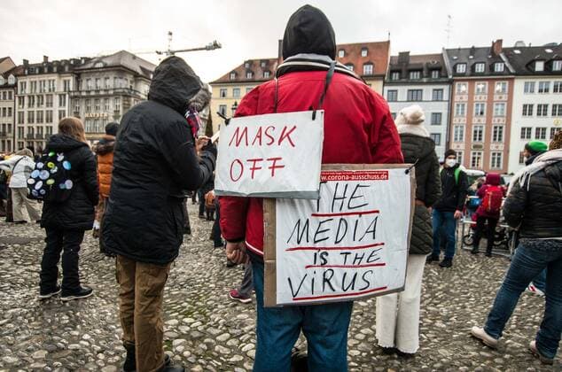 November 28, 2021, Munich, Bavaria, Germany: A pandemic denier in Munich, Germany wears a sign indicating mistrust of the media in calling it the virus and on another sign indicates being an anti-masker. Despite southern Bavaria being in the clutches of a brutal fourth wave and beingnonnthe cusp of a Delta and Omicron Winter, Corona deniers from throughout Germany banded together without respecting any of the infection control regulations to memorialize disgraced former police officer and conspiracy theorist Karl Hilz who died after being reported by those in his circles as a pneumonia . Since Hilz s death, numerous grifters from the Querdenker scene with little to no connection to him have claimed knowing him and have even tried to - ZUMAb160 20211128_zbp_b160_037 Copyright: xSachellexBabbarx