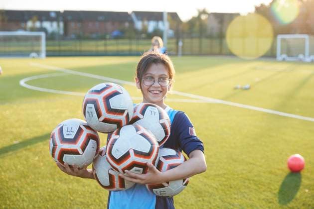 UK, Smiling female soccer player (10-11) holding balls in field UK, Smiling female soccer player holding balls in field