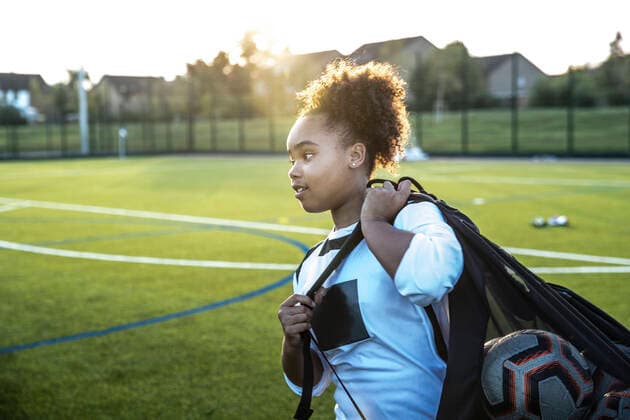 IMAGO Creative: Internationaler Frauenmonat, Mädchen im Sport Creative Highlights Symbolbilder UK, Rear view of female soccer player (12-13) carrying bag with balls in field UK, Rear view of female soccer player carrying bag with balls in field