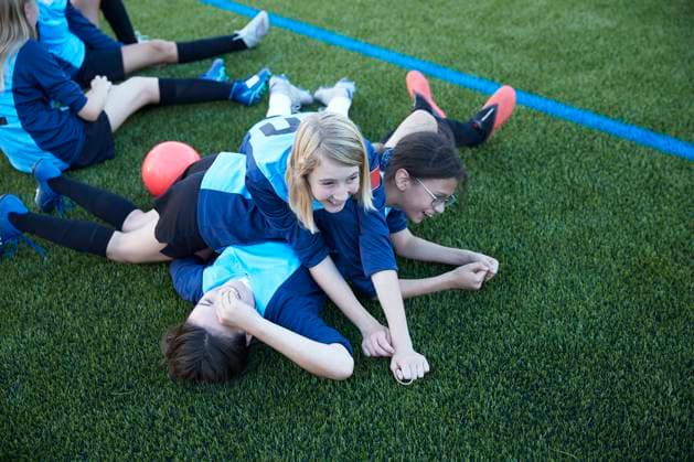 UK, Playful female soccer players (10-11, 12-13) lying in field UK, Playful female soccer players lying in field