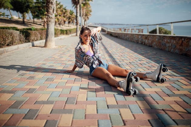 IMAGO Creative, Jahreszeit Sommer, Sommer in der Stadt Full body side view of sportive female in roller skates sitting on colorful paved pathway on street with tall trees DaniNavarro_RollerSkaterYoungWoman_4.jpg Copyright: xDanixNavarrox Model Released