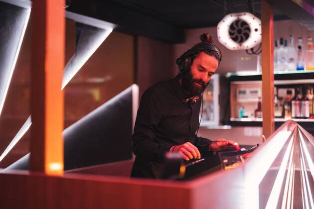 IMAGO Creative: Guten Rutsch Concentrated young bearded male DJ in headphones standing at illuminated counter in modern nightclub JavierDeLaTorre_DJTeatre_27.jpg Copyright: xJavierxDexLaxTorrex Model Released