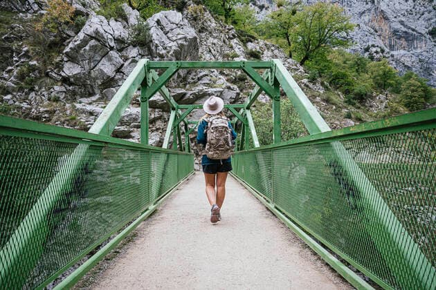 Creative Highlights Symbolbilder Back view of unrecognizable female traveler with backpack strolling on narrow bridge and admiring landscape of high steep mountains, Model released JoseLuisCarrascosa_WomanAtPicosDeEuropa_6.jpg Copyright: xJosexLuisxCarrascosax MR