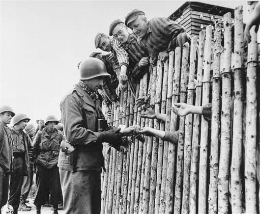 U.S. Army Corporal Larry Matinsk puts cigarettes into the extended hands of newly liberated prisoners behind a stockade in the Allach concentration camp, near Dachau Germany on April 30, 1945. Also pictured are U.S. Army Soldiers Arthur Toratti and George Babel (second and third from the left). Allach was a subcamp of the Dachau concentration camp. American Soldiers of the U.S. 7th Army, including members of the 42nd Infantry and 45th Infantry and 20th Armored Divisions participated in the subcamp™s liberation. The main concentration camp at Dachau had more than 120 subcamps in the area . . 1062_33_L_-10385-