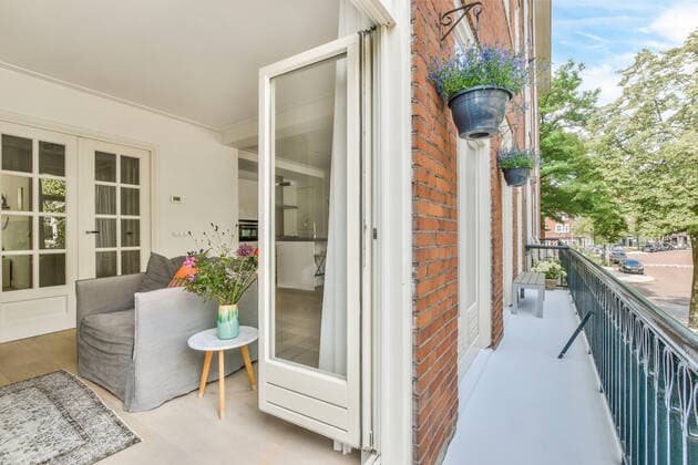 Living room with armchair and flowers near opened balcony door with metal fence and brick wall of building located on street CasaMedia_Waalstraat52-1_9.jpg Copyright: xCasaxMediax Model Released