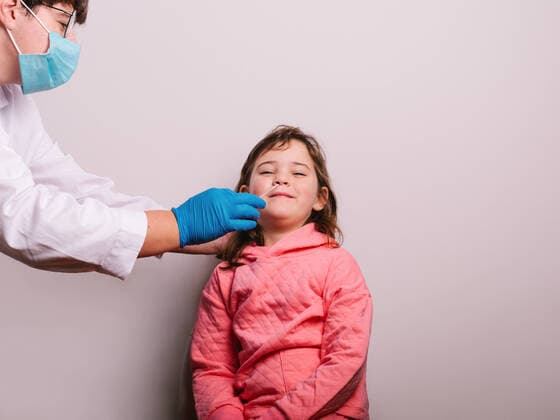 Creative Highlights Symbolbilder Side view crop medical practitioner in uniform and glove doing COVID 19 swab test to cheerful girl with smile against gray wall, Model released HodeiUnzueta_TestCovid_4.jpg Copyright: xHodeixUnzuetax MR