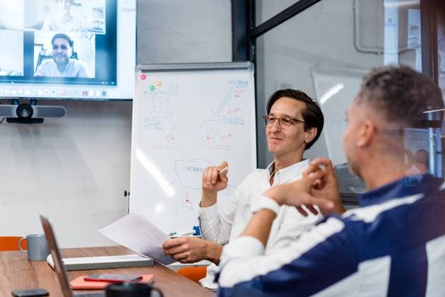 Coworkers sitting at table with gadgets and documents in modern workspace with white flip chat during online conference in office, Model released, Property released JakeJakab_AreaCoworking_57.jpg Copyright: xJakexJakabx MR