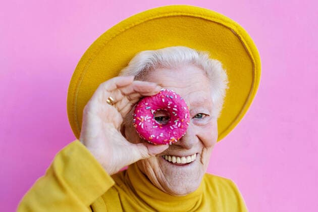 Creative Highlights Symbolbilder Happy elderly female with gray hair in stylish yellow hat covering eye with sweet glazed round doughnuts on pink background, Model released SergioVictorVega_TitiFishes_11.jpg Copyright: xSergioxVictorxVegax MR
