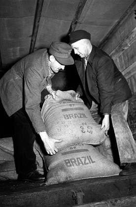 Brazilian coffee and workers in a lorry: Historical image Two men carry a bag of Brazilian coffee on load area of a lorry, 1952. Historical image from GDR. German Democratic Republic. East Germany.