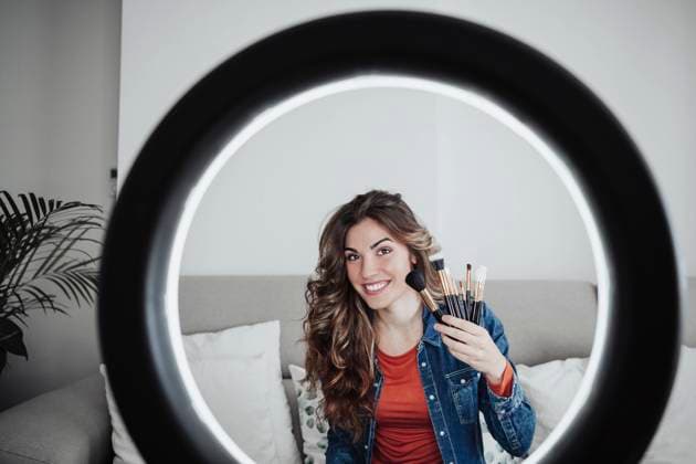 IMAGO Creative: Digitale Welt, Social Commerce Smiling influencer with make-up brushes seen through ring light model released property released, EBBF04871