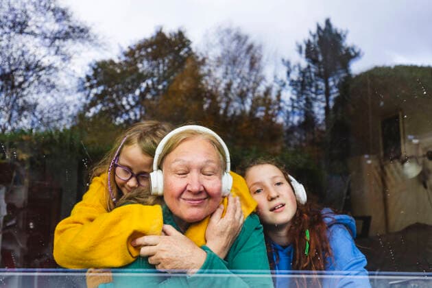 Girls embracing grandmother listening music through headphones at home model released property released, IHF00622