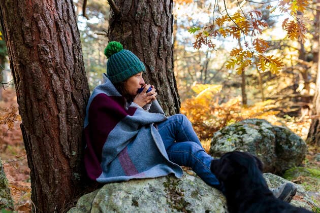 IMAGO Creative: Internationaler Frauenmonat, Gesundheit, Frauen in der Menopause Woman wrapped in blanket drinking coffee sitting on rock by dog at forest model released property released, MRRF01737