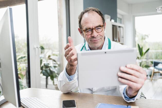 Smiling doctor with digital tablet gesturing on video call at clinic model released property released, UUF25259