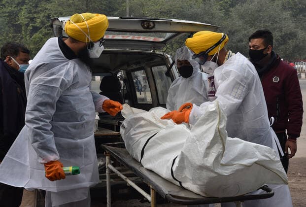 NEW DELHI, INDIA - JANUARY 13: Shaheed Bhagat Singh Sewa Dal volunteers in personal protective equipment (PPE) take out from a hearse the body of a person who died due to the Covid-19 coronavirus, at a cremation ground at crematorium Center Old Seema Puri Ghat, on January 13, 2022 in New Delhi, India. (Photo by Sonu Mehta Hindustan Times ) Daily Life Amid Coronavirus Pandemic In India