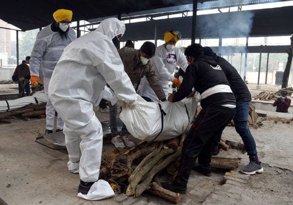 NEW DELHI, INDIA - JANUARY 13: Shaheed Bhagat Singh Sewa Dal volunteers in personal protective equipment (PPE) take out from a hearse the body of a person who died due to the Covid-19 coronavirus, at a cremation ground at crematorium Center Old Seema Puri Ghat, on January 13, 2022 in New Delhi, India. (Photo by Sonu Mehta Hindustan Times ) Daily Life Amid Coronavirus Pandemic In India