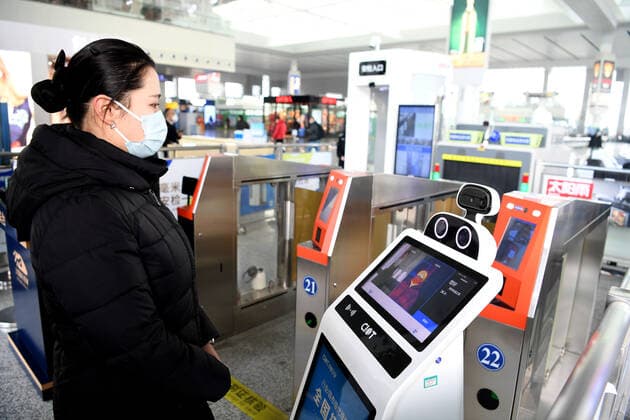 (211219) -- HEFEI, Dec. 19, 2021 -- Da Bai (R), an intelligent temperature measuring robot, measures a passenger s body temperature at the entrance of Hefei South Railway Station in Hefei, east China s Anhui Province, Jan. 18, 2022. Air environment automatic sterilizer robot Xiao Chuang, intelligent temperature measuring robot Da Bai and ground cleaning and disinfecting robot Xiao De have been in service for COVID-19 prevention and control during the annual Spring Festival travel rush in Hefei. ) CHINA-ANHUI-RAILWAY STATION-ROBOTS (CN) LiuxJunxi 