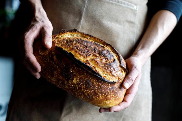 Baker wearing apron holding freshly baked sourdough bread loaf model released property released, IFRF01294
