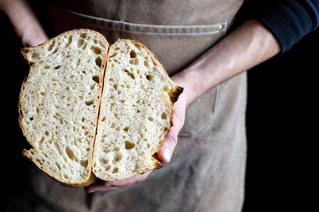 Baker holding halved loaf of bread at bakery model released property released, IFRF01296