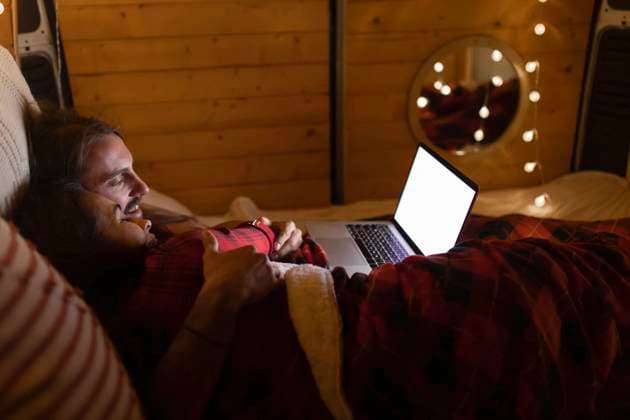 IMAGO Creative, Weihnachten, Tradition: Weihnachtsfilme sehen Couple using laptop lying on bed in camper van model released property released, EGHF00305