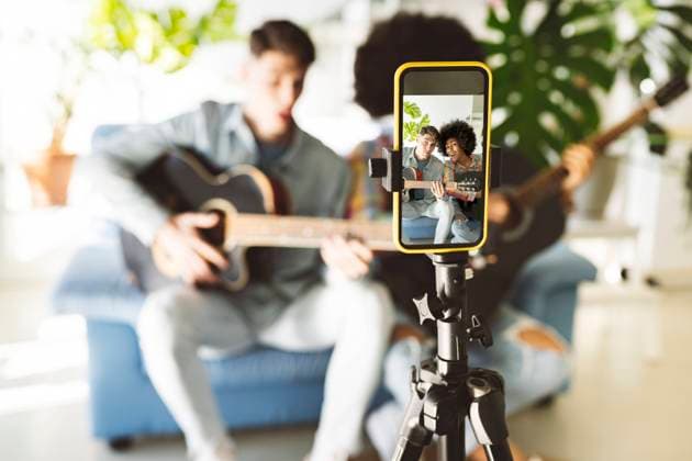 Young couple playing guitar together vlogging through smart phone at home model released property released, JCCMF05035
