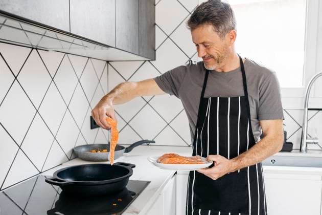 Smiling man cooking fish in kitchen at home model released property released, JRFF05250