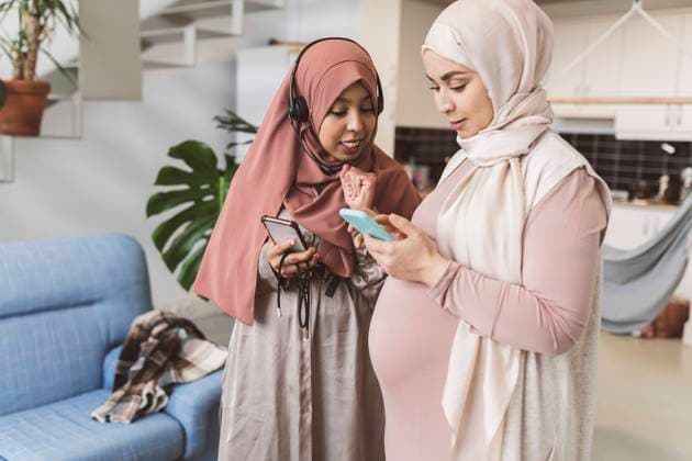 Pregnant woman sharing smart phone with friend in living room model released property released, JCCMF05117