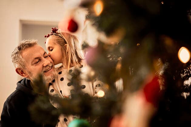 IMAGO Creative: Countdown bis Weihnachten, Nach Hause reisen Granddaughter kissing grandfather behind christmas tree at home model released property released, ZEDF04419