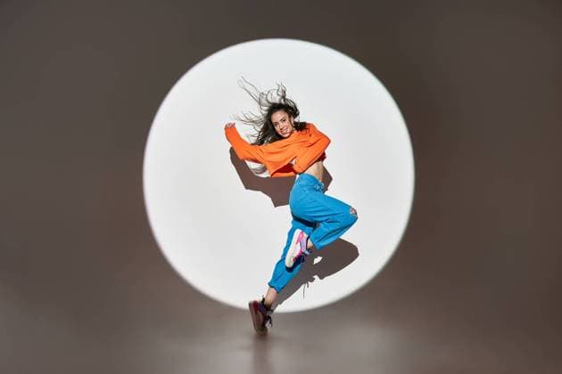 Side view of energetic happy female dancer jumping with raised leg and outstretched arms in light of projector in studio looking at camera, Model released ManuelRuiz_DancerWhiteStudio_05.jpg Copyright: xManuelxRuizx MR
