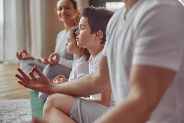 Calm little boy enjoying meditation with family indoors Cropped head of smiling woman watching her husband and kids doing mental practice at home together Copyright: xx 40580950