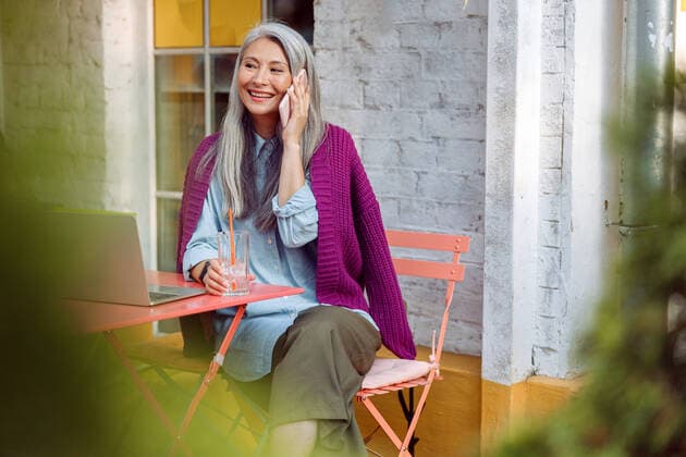 IMAGO Creative: Urban Diversity Positive senior lady with glass of water talks on cellphone sitting at table with laptop Positive senior Asian lady with glass of water talks on cellphone sitting at table with laptop on outdoors cafe terrace Copyright: xyaroslavxastakhovx 41037544