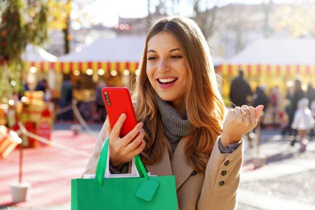 Attractive excited young woman watching smartphone and holding shopping bags walking in the Christmas Markets Copyright: xx 43433884