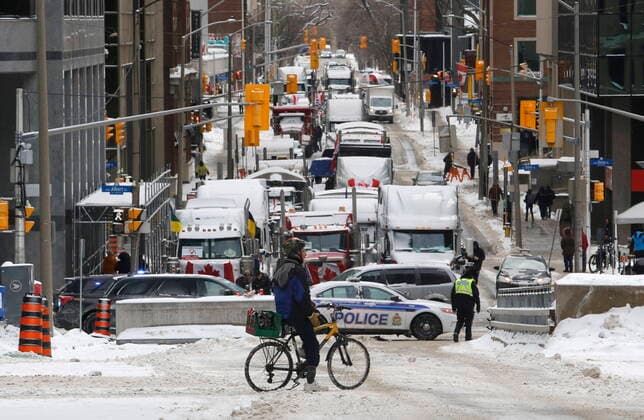 February 4, 2022, Ottawa, ON, Canada: A cyclist stops in front of trucks blocked on Metcalfe Street as a rally against COVID-19 restrictions, which began as a cross-country convoy protesting a federal vaccine mandate for truckers, continues in Ottawa, on Friday, February 4, 2022. Ottawa Canada  - ZUMAc35_ 20220204_zaf_c35_143 Copyright: xPatrickxDoylex