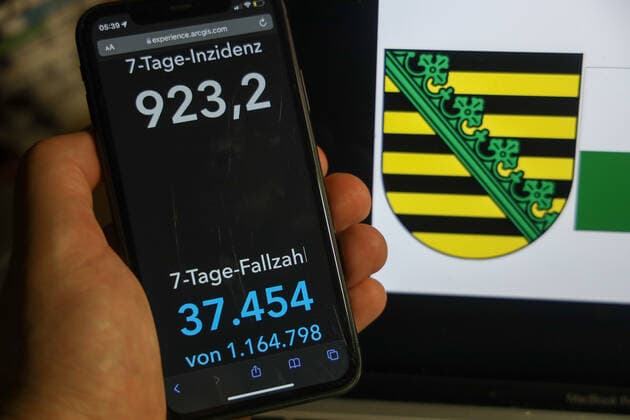 Coronavirus in Deutschland - Covid-19-Dashboard des Robert Koch-Institut DEU, Deutschland, Sachsen 06.02.2022: Die 7-Tage-Inzidenz für das Bundesland (Fälle letzte 7 Tage 100.000 EW) wird auf einem iPhone angezeigt, im Hintergrund das Landeswappen
