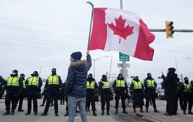 February 12, 2022, Windsor, ON, CANADA: A supporter waves a Canadian flag on a hockey stick as police officers enforce an injunction against their demonstration, which has blocked traffic across the Ambassador Bridge by protesters against COVID-19 restrictions, in Windsor, Ont., Saturday, Feb. 12, 2022. Windsor CANADA  - ZUMAc35_ 20220212_zaf_c35_115 Copyright: xNathanxDenettex