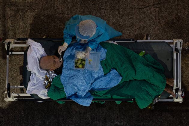 Hong Kong s COVID-19 Infections Soar On February 16, 2022, a patient lies in a hospital bed waiting for medical treatment in a temporary holding area outside Caritas Medical Center in Hong Kong, China, while medical staff feed the patient. The Food and Health Bureau confirmed a new record of 4,285 infections, while 7,000 people initially tested positive, a near-record high. At least 12,000 infected people are waiting to be admitted to hospitals as COVID-19 cases overwhelm the public health system. Hong Kong China  Copyright: xLeungxManxHeix originalFilename: manhei-notitle220216_npTyk.jpg