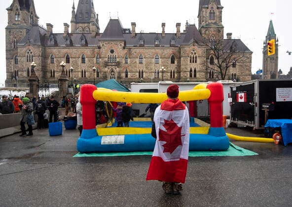 February 17, 2022, Ottawa, ON, CAN: A protester wearing a Canadian flag takes a photo of children playing in an inflatable bouncy castle on Wellington Street across from ParliamentöÄÃ s West Block on the 21st day of a protest against COVID-19 measures that has grown into a broader anti-government protest, in Ottawa, on Thursday, Feb. 17, 2022. Ottawa CAN  - ZUMAc35_ 20220217_zaf_c35_075 Copyright: xJustinxTangx