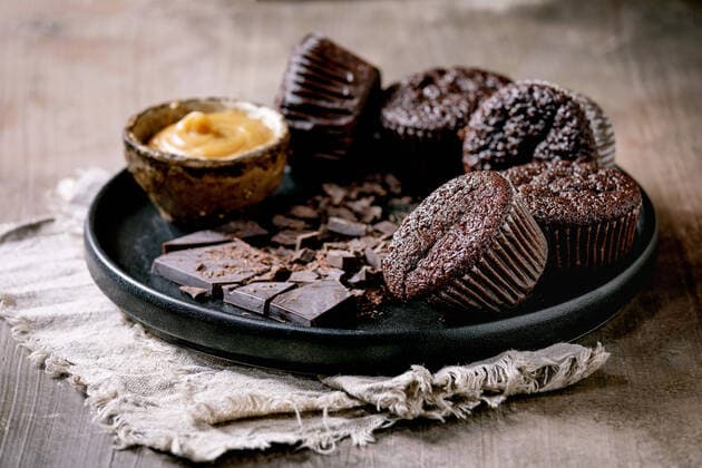 Homemade chocolate cupcakes muffins with salted caramel sauce and chopped dark chocolate on black ceramic plate over concrete texture background. NatashaBreen REDA&CO 1028_29_NBR09761