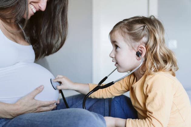 IMAGO Creative: Mutterschaft Curious girl listening to pregnant mother s belly through stethoscope model released property released, EBBF05231