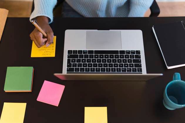Businesswoman writing on adhesive note at desk in home office model released property released, PNAF03048