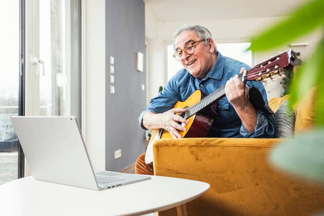 Senior man learning guitar through online tutorial on laptop at home model released property released, UUF25345