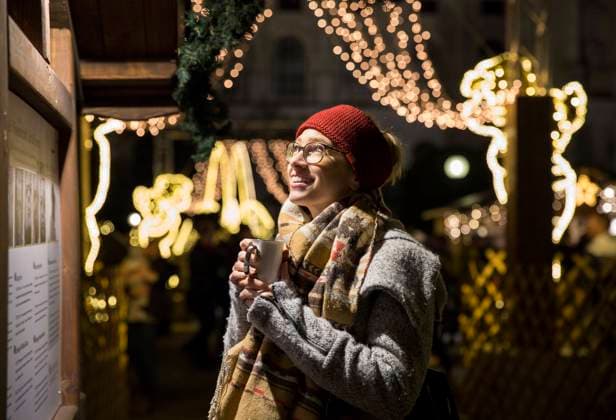 Young woman holding cup by decorated stall at Christmas market Young woman holding cup by decorated stall at Christmas market