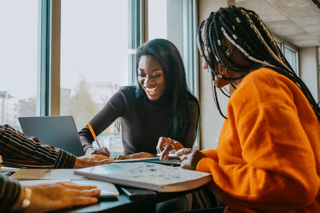 IMAGO Creative: Bildung, Schreiben Cheerful female friends studying together while sitting at table in college cafeteria Germany, Berlin, model released, property released Copyright: xMaskotx , MA92298