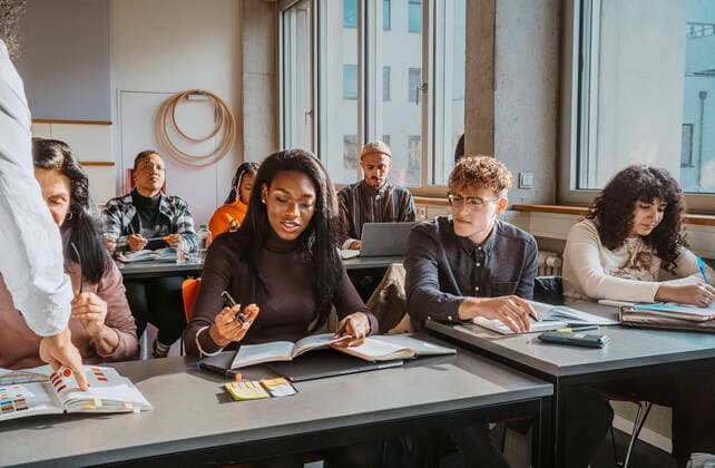 Multiracial students sitting at desk while learning from professor in classroom Germany, Berlin, model released, property released Copyright: xMaskotx , MA92350