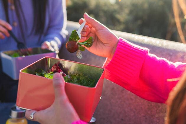 Creative Highlights Symbolbilder Side view of anonymous cheerful Hispanic female friends eating salad while sitting on stone bench with water bottles on sunny street DavidMunoz_JenniferAndAlejandraLifestyle_5.jpg Copyright: xDavidxMunozx Model Released