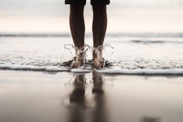Creative Highlights Symbolbilder Crop anonymous barefoot male tourist standing on shore with splashing foamy sea during trip in coastal area of Canary island, Model released PabloMenendez_TenerifeTrip_62.jpg Copyright: xPabloxMenendezx MR
