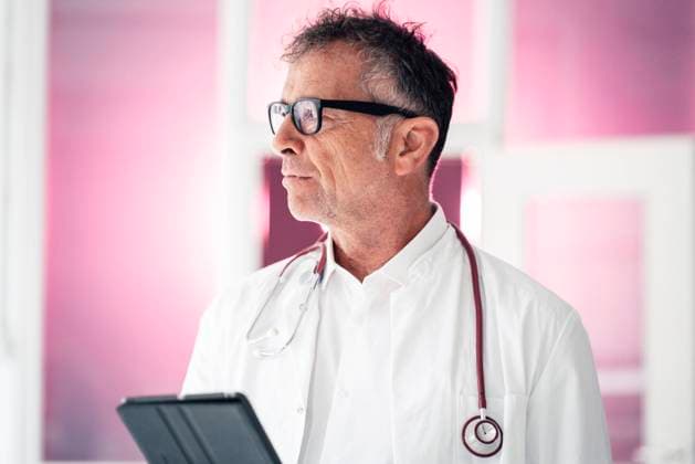 IMAGO Creative: Lokalhelden - Gesundheits- und Rettungskräfte Thoughtful doctor with tablet PC standing in clinic model released property released, JOSEF07270