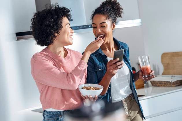 Young woman feeding cereal to friend standing in kitchen at home model released property released, JSRF01913