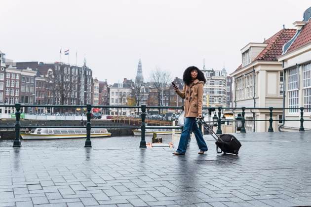 IMAGO Creative: Welttourismustag am 27. September Woman with smart phone pulling wheeled luggage walking on footpath in city model released, PNAF03364